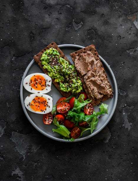 Delicious breakfast, tapas, snack - crispy rye bread with turkey liver, avocado, boiled egg and vegetable salad on a dark background, top view Delicious breakfast, tapas, snack - crispy rye bread with turkey liver, avocado, boiled egg and vegetable salad on a dark background, top view egg cherry tomato rye stock pictures, royalty-free photos & images