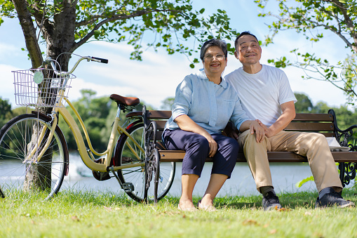 Happy and healthy couple Asian sitting chair beside a bicycle Family and friendship lifestyle, Enjoyment of active seniors, and outdoor activity after retirement, health care insurance concept