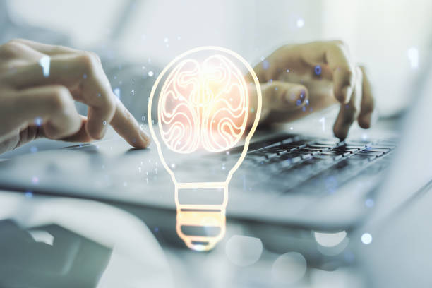 istock Creative light bulb with human brain hologram and with hands typing on computer keyboard on background, artificial Intelligence and neural networks concept. Multiexposure 1899074170