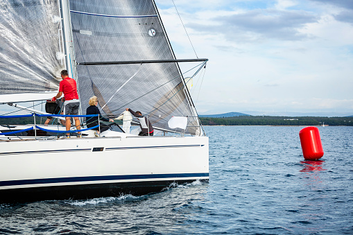 Sailing crew on sailboat making turn on buoy on regatta. Models and event regatta property released.