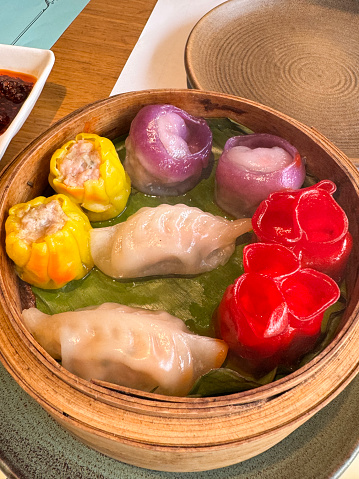 Stock photo showing elevated view of a portion of multicoloured momos served in a bamboo steamer, shell shaped dumplings similar to wontons and gyoza, a popular Indian street food.