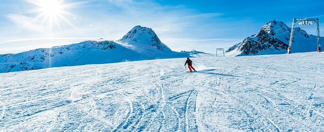 Adult skier skiing down the slope of ski resort on sunny winter day.