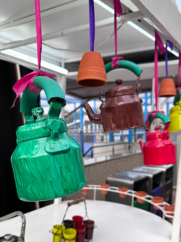 Stock photo showing a row of multicoloured, painted metal tea kettles hanging on colourful ribbons over a street masala tea kiosk stall. The decorations are designed to draw the attention of potential customers.