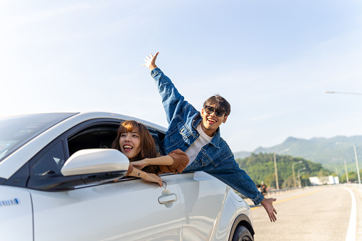 Group of Happy Asian man and woman enjoy and fun outdoor lifestyle road trip travel on summer holiday vacation. Generation z people friends sitting in the car looking beautiful nature of countryside.