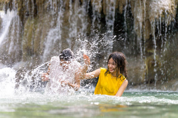 Group of Young Asian man and woman enjoy and fun outdoor lifestyle travel nature tropical forest mountain on summer holiday vacation. Happy generation z people friends playing water together at waterfall.