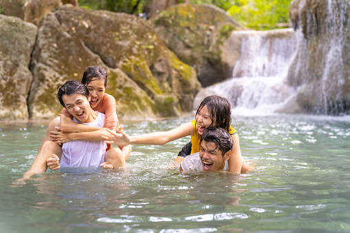 Group of Young Asian man and woman enjoy and fun outdoor lifestyle travel nature tropical forest mountain on summer holiday vacation. Happy generation z people friends playing water together at waterfall.