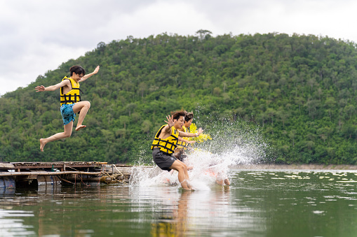 A small group of three children are seen in mid air jumping off the end of a dock on a sunny summer day. They are each striking a fun pose before they hit the waters surface to make a splash.