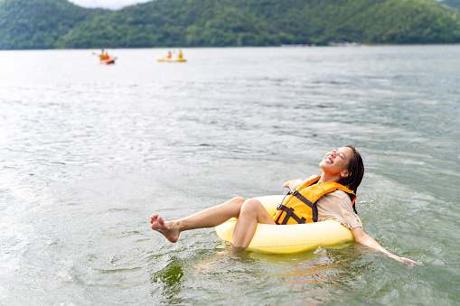 Young Asian woman with life vest and swim ring playing water in the lake. Happy generation z people enjoy and fun outdoor lifestyle travel nature forest mountain lake house on summer holiday vacation.