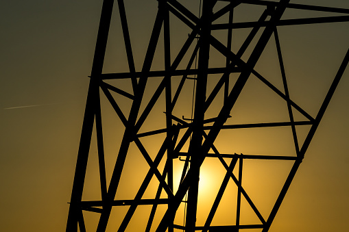 Base of a pylon carrying high voltage cables with the orange summer sunset as a background
