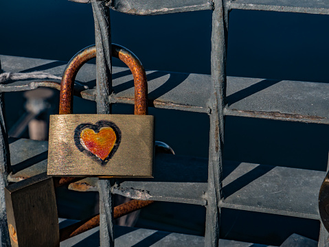 A close up macro shot of a red lock that has an engraved heart on it, locked on a fence