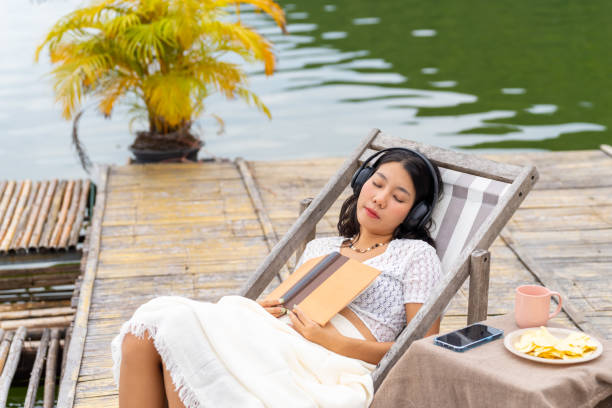 mulher asiática nova que relaxa na varanda da casa do lago. - balcony beach book men - fotografias e filmes do acervo