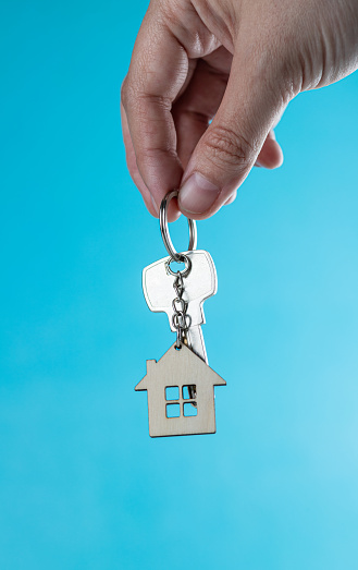 The hand holds a key with a keychain in the form of a house on a blue background