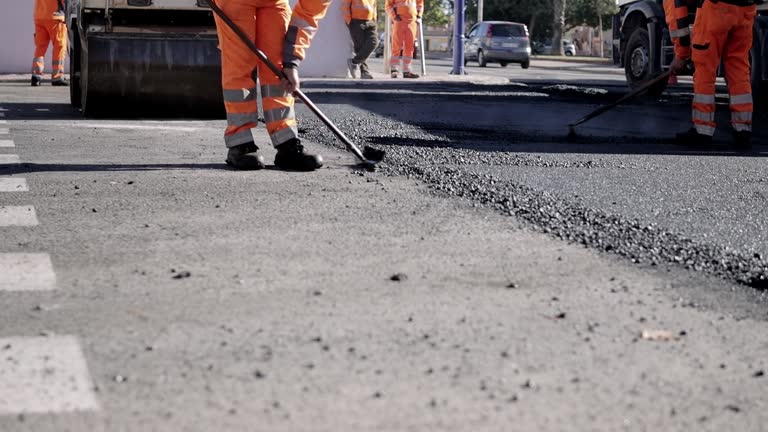 Road workers in protective clothing are repairing the asphalt surface of the streets with hot asphalt, close-up on the workers' feet, slow motion