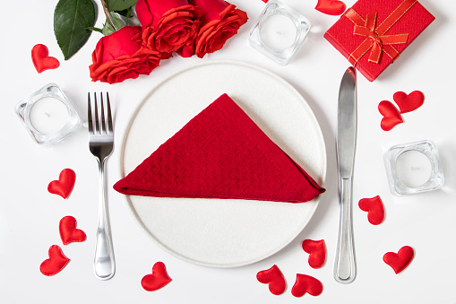 Table setting for valentine's day. Red roses and cutlery on white background.