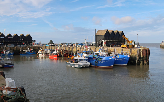 Whitstable, Kent, United Kingdom, December 29, 2023. Quaint traditional harbour waterfront with fishing boats or trawlers. Sunny winter day outdoors