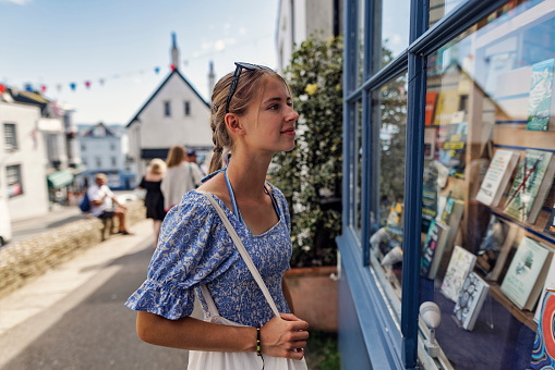 Teenage girl enjoying summer vacations in Dorset, United Kingdom. 
She is walking in the beautiful street in the old town of Lyme Regis. The girl is looking at the books in the local bookstore.
Sunny summer day.
Shot with Canon R5