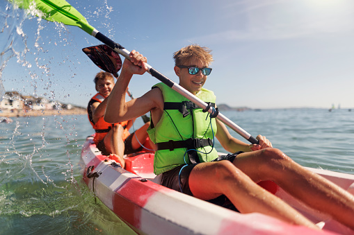 Teenagers enjoying summer vacations in Lyme Regis, Dorset, United Kingdom.\nThey are kayaking in the sea on sunny summer day.\nCanon R5