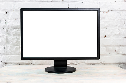 Computer monitor on a table against brick wall, blank white screen