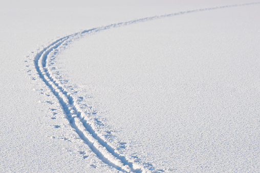 Ski tracks in snow on a frozen lake in Bergen, Norway in winter left by a cross country skier. The skier has made a curve in the snow surface.