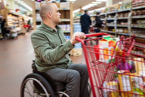 A man of Caucasian descent with a physical disability, using wheelchair pushes a shopping cart in a local grocery store in Central Oregon.