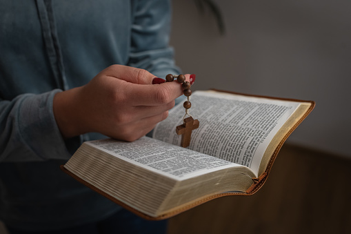 female hands holding bible, rosary with wooden cross during prayer.
