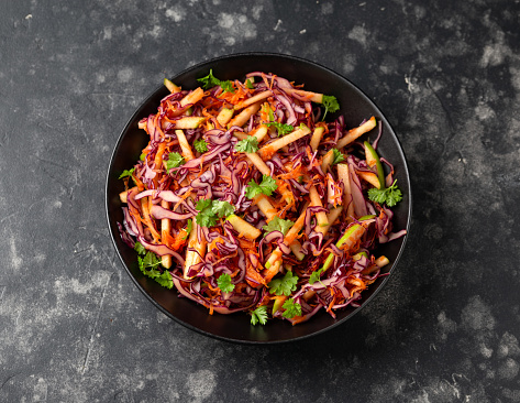 Red Cabbage salad with apples and carrots in black bowl.