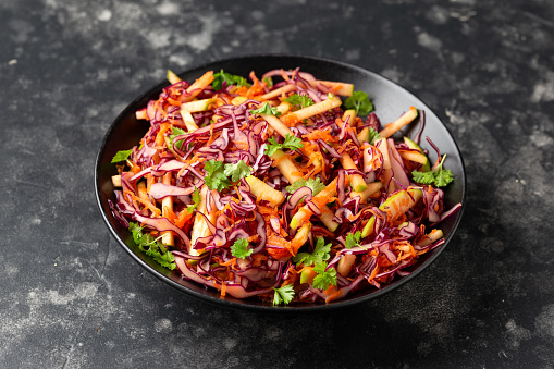 Red Cabbage salad with apples and carrots in black bowl.