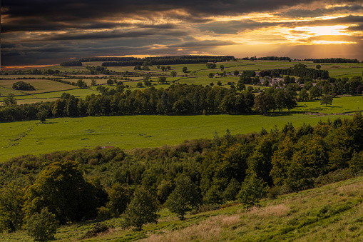 Digital composite of sunset view of fields and trees in the Lake District of Cumbria, England from the top of a hill.