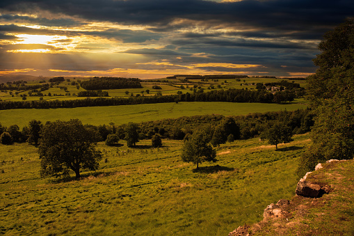 Digital composite of sunset view of fields and trees in the Lake District of Cumbria, England from the top of a hill.