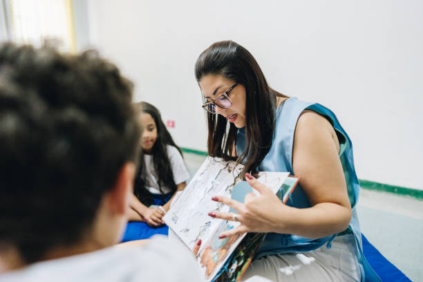 istock Teacher reading a book to her student at school 1899575063