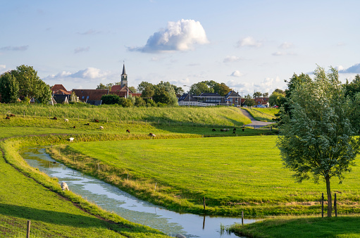 Small village with a church with a grassy polder and a canal. Location is Driehuizen, Netherlands