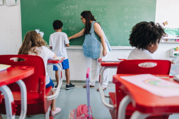 istock Teacher teaching her student on classroom chalkboard at school 1899648838