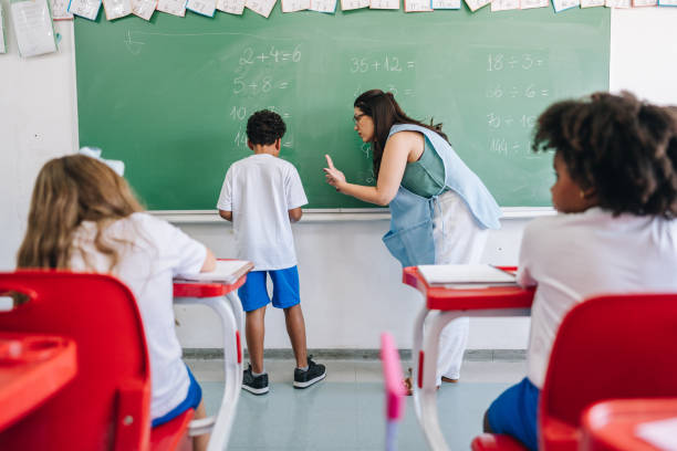 istock Teacher teaching her student on classroom chalkboard at school 1899648845