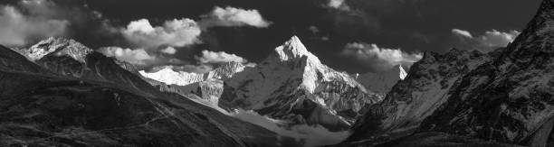 White fluffy clouds in high altitude skies over the snow capped peak of Ama Dablam, deep in the Himalayan mountain wilderness of the Everest National Park, Nepal.