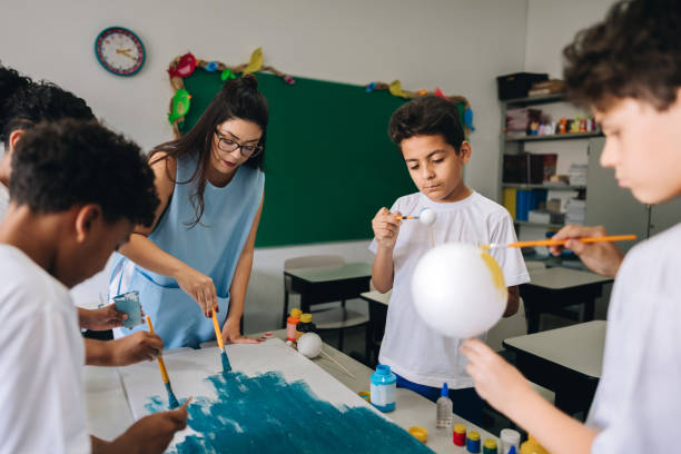 istock Teacher helping her students with paint on classroom at school 1899700526