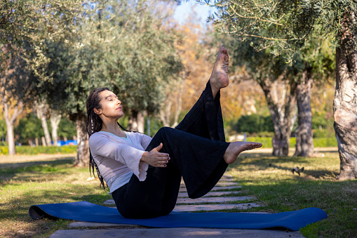 young woman performing yoga in the green garden, practicing boat pose