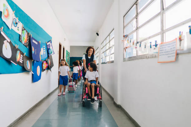 istock Teacher pushing student using wheelchair on corridor at school 1899723162