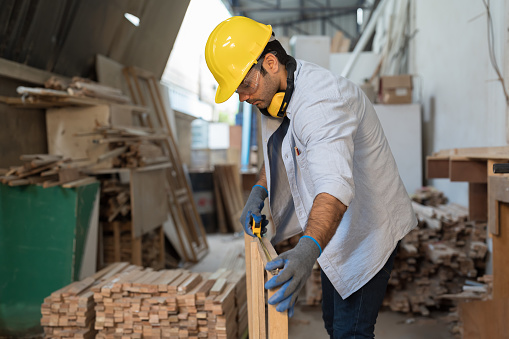 Male carpenter checking piece of wood. Builder worker working with wood. Male construct making furniture in factory woodwork. Concept of wood industrial factory