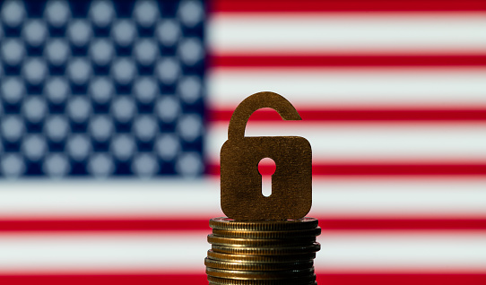 Symbolic lock with a keyhole and a column of coins on the background of the USA flag