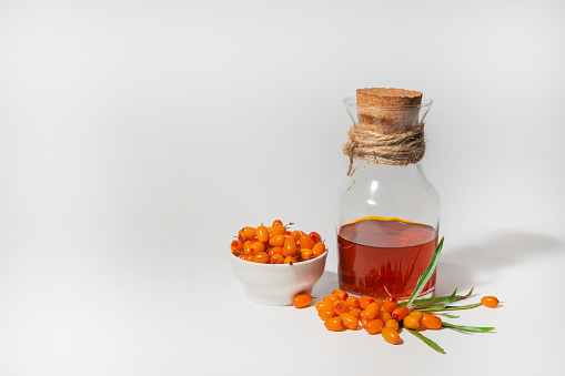 A bottle of sea buckthorn oil and sea buckthorn berries on a white background. Healing oil making concept.