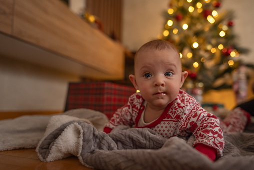 Cute baby girl crawling on the floor with the Christmas tree in the background