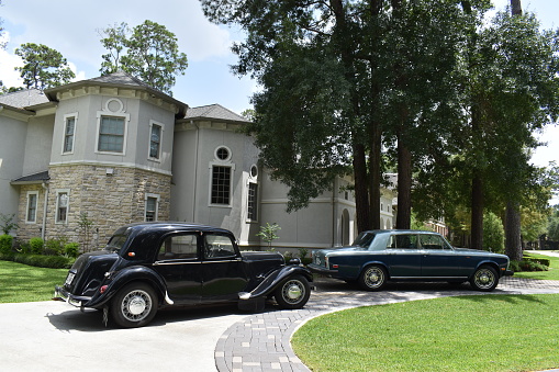 Houston, TX USA 07-27-2023 - Portrait of a black 1925 Rolls-Royce Phantom, a blue (two toned) 1972 Rolls-Royce Silver Shadow and a luxurious mansion.