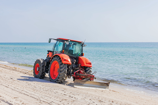 Close-up view of a tractor driving along the Atlantic Ocean coastline, leveling the sand. Miami Beach. USA.