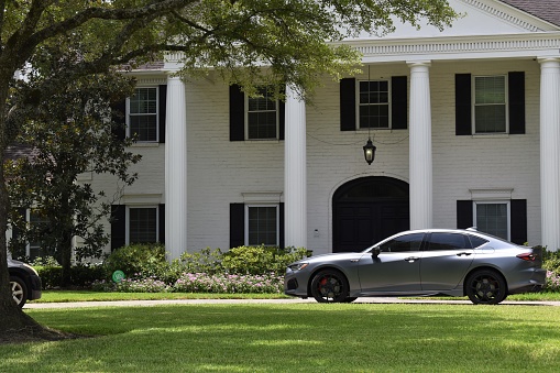 Houston, TX USA 07-27-2023 - A luxurious mansion with a silver-gray colored Acura TLX parked in the driveway.