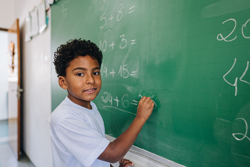 Portrait of a student boy writing on chalkboard in classroom at school