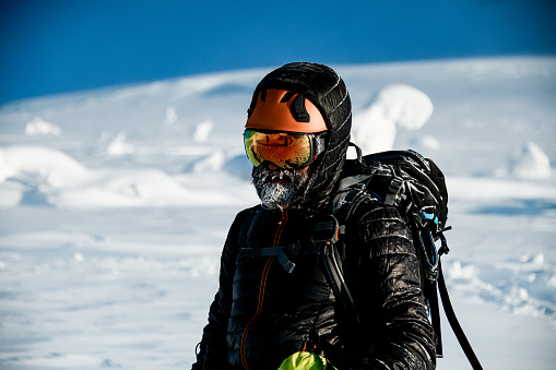portrait of adult man with a frozen icy beard in bright helmet and goggles and black jacket