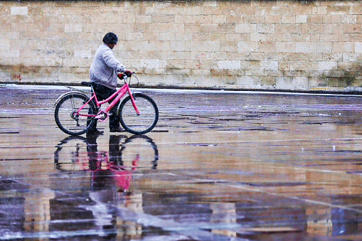 Karaman, Turkey, January 24, 2018: A man trying to go home with his pink bicycle after the rain in Aktekke square