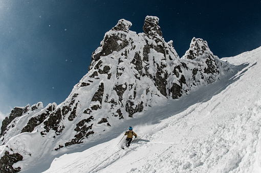 professional freeride skier riding down on steep snowy mountain on a sunny day. Blue sky on the background