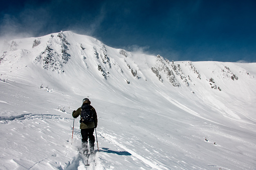 rear view of skier with backpack going up the snowy mountain. Ski touring and freeride concept