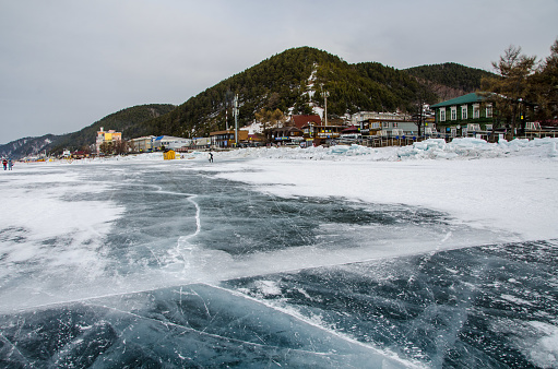 Cracked winter lake Baikal with transparent ice, mountainous touristic background